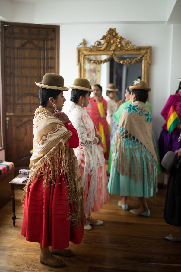 A group of Aymara women in traditional dress, inspecting themselves in a mirror.