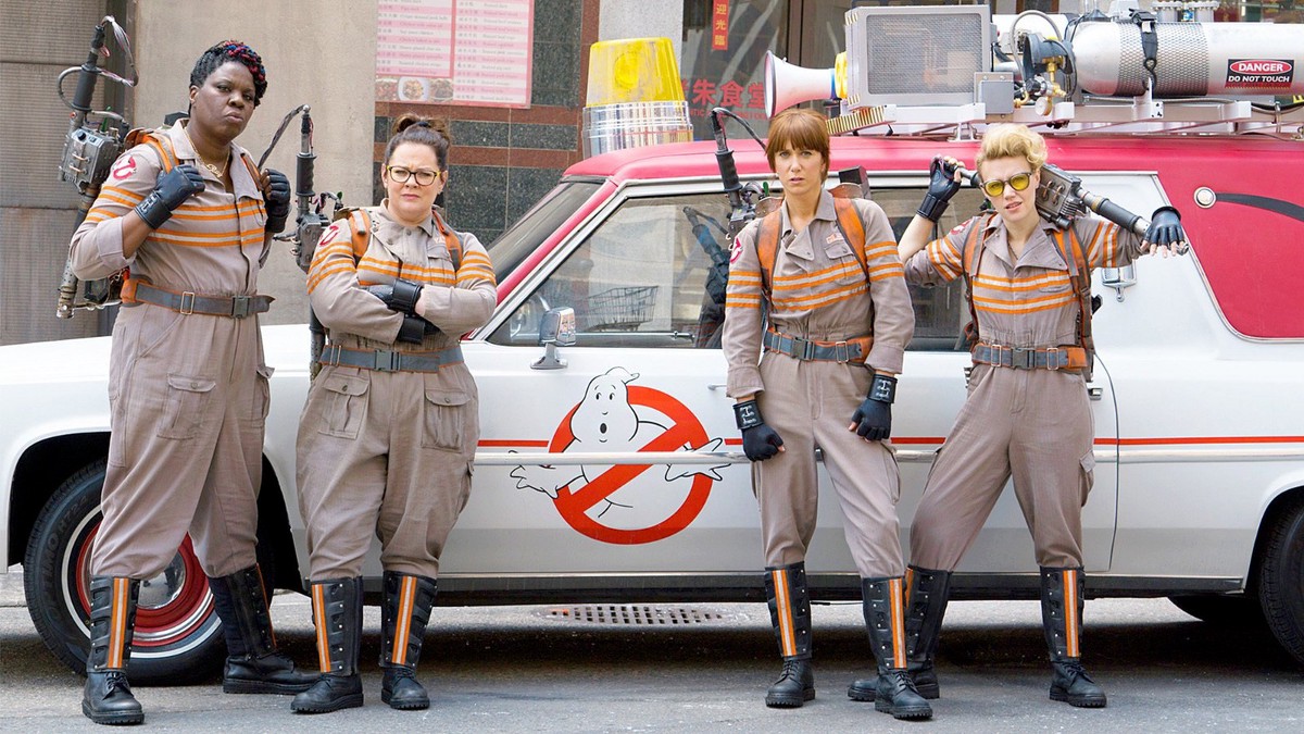 The cast of the 2016 movie Ghostbusters stand in front of the movie's signature red and white converted hearse.