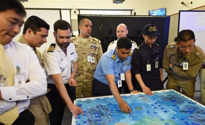 A group of people in uniform gather around a large game board, discussing moves.