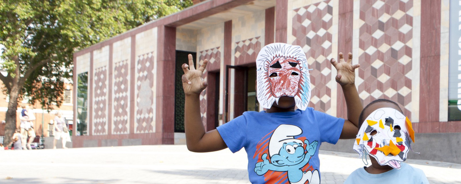 A child wears a crayon lion mask outside of a museum.