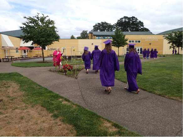 Students in graduation gowns and caps walking across a campus.