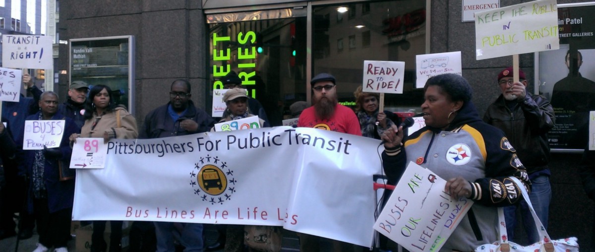 Protesters from Pittsburghers for Public Transit hold a banner outside an office.