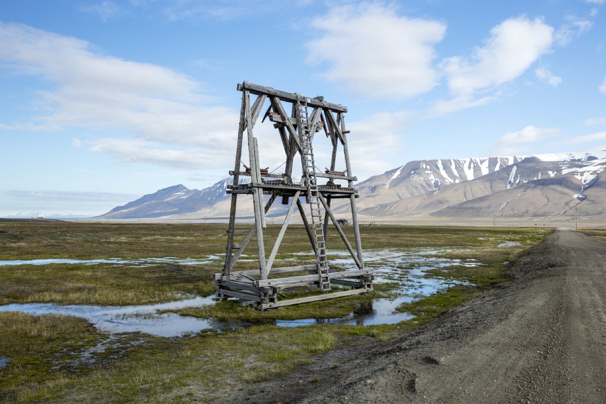 A large triangular wooden structure in an otherwise empty marshy flatlands, with mountains in the distance.