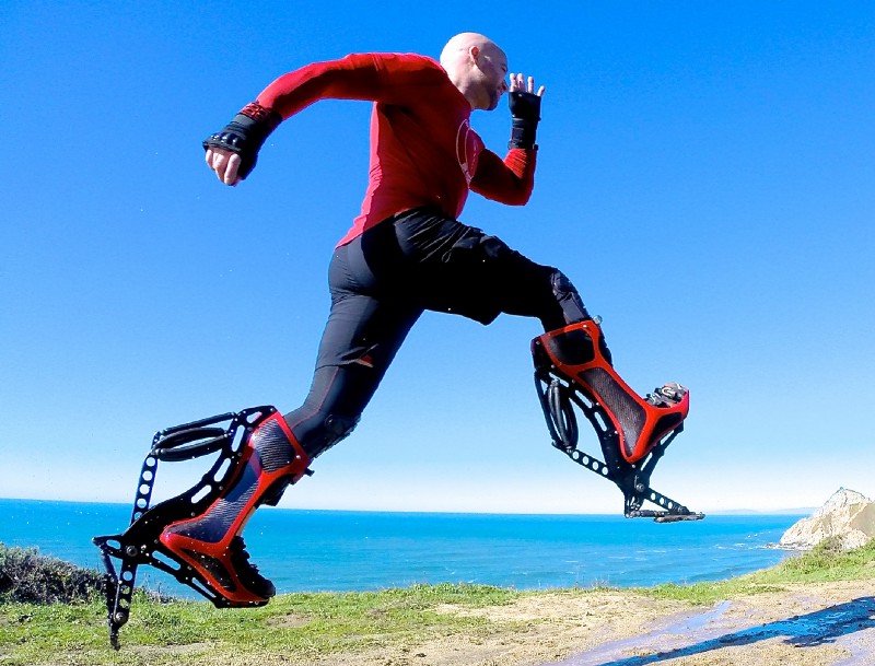 A man jumps through the air while wearing bright red boots that have jacksprings attached to the bottoms.