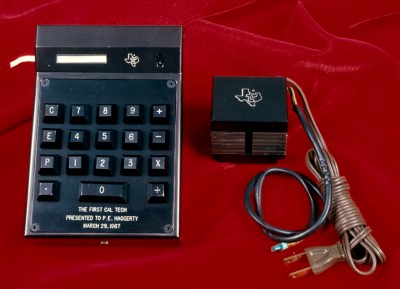 A black calculator with a large power plug attachment.