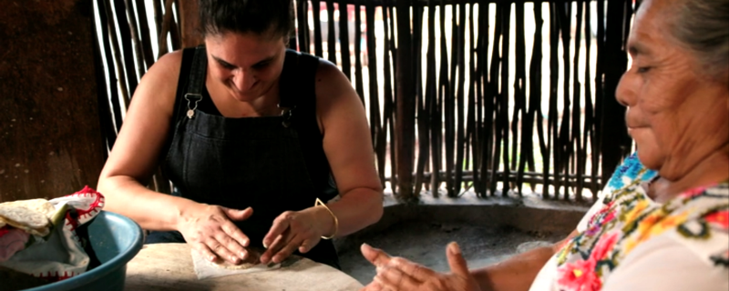Two women make tortillas by hand.