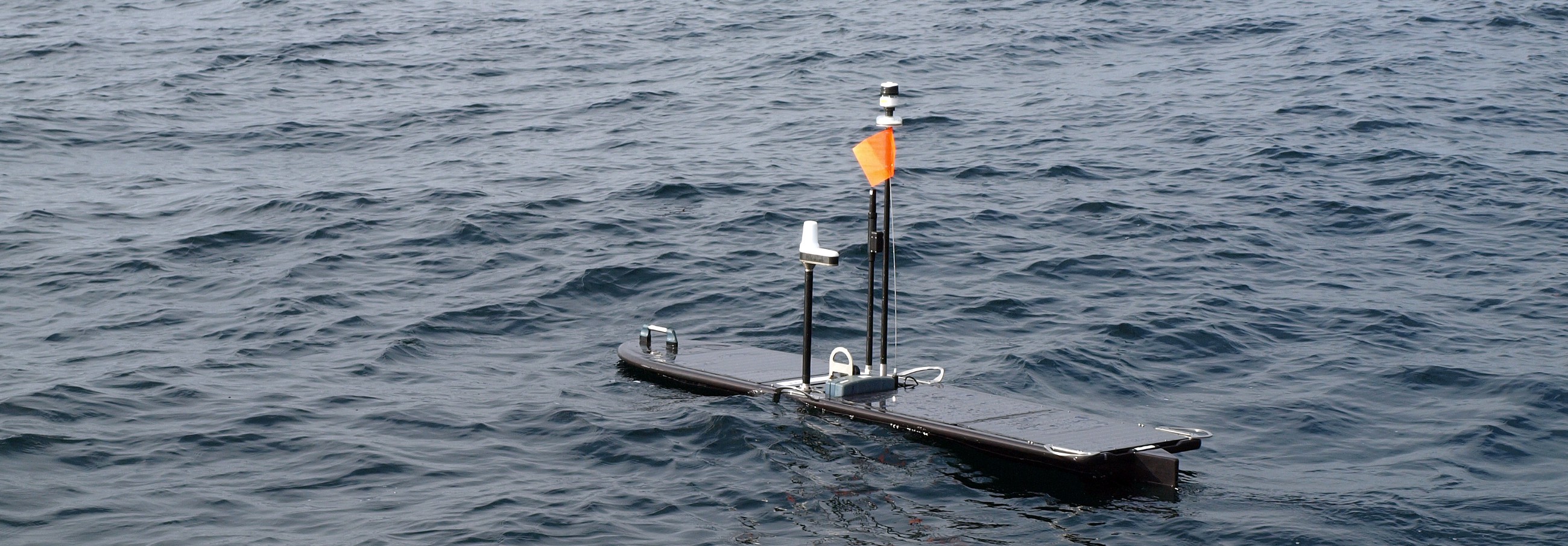 An autonomous underwater drone floats at the surface of the sea, with its antennae and top deck poking above the waves.